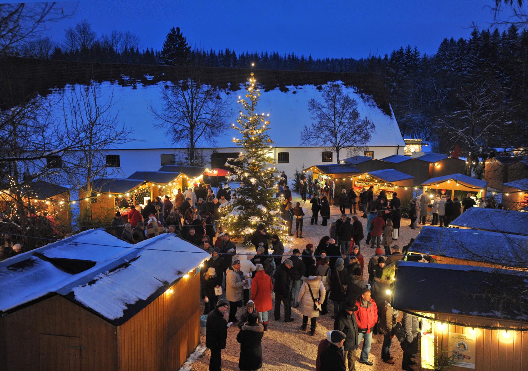 Nachtaufnahme im Vordergrund beleuchtet Buden des Weihnachtsmarktes